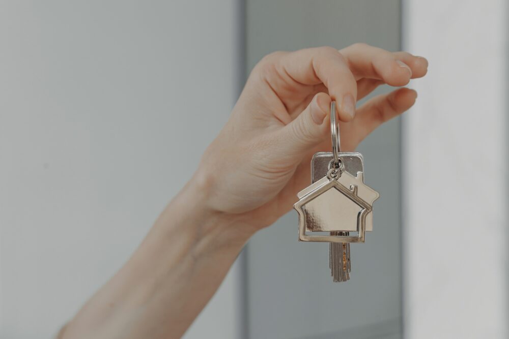 Hand presenting keys with a charming house keychain, offering new home.